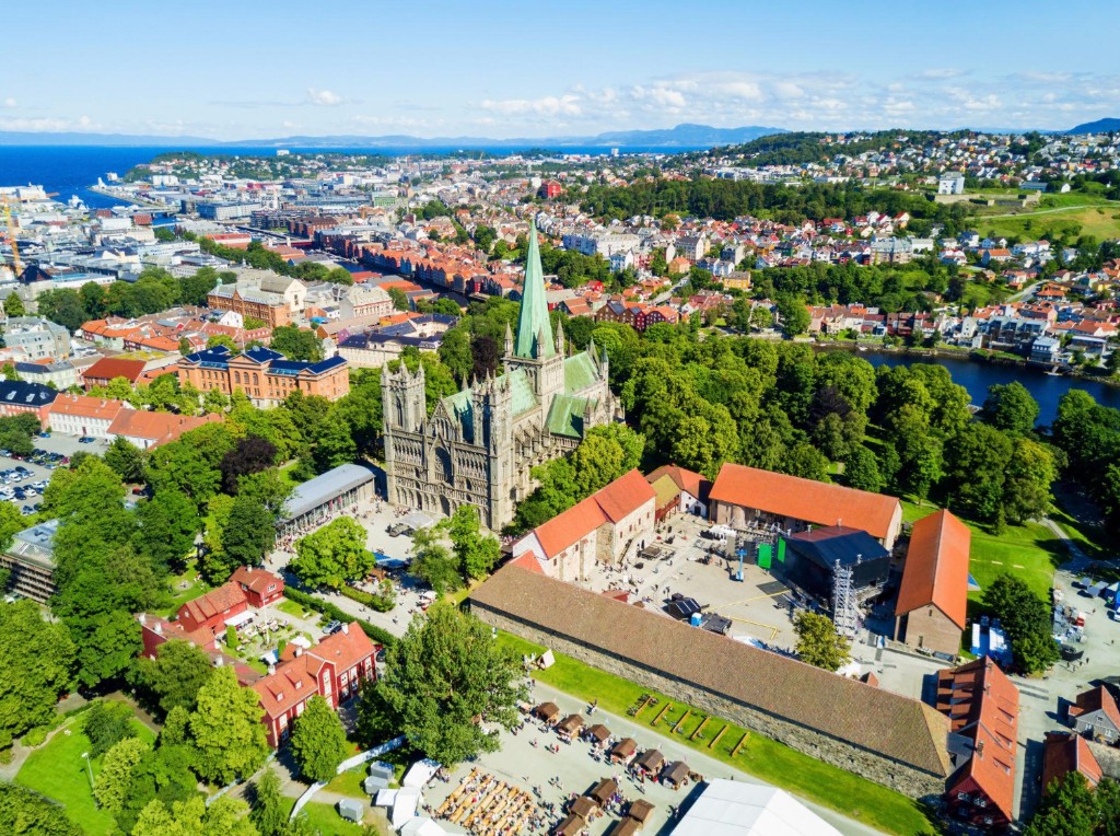 Aerial view of Trondheim with Nidaros Cathedral, green spire, historic red-roofed buildings, and Trondheimsfjord in the background